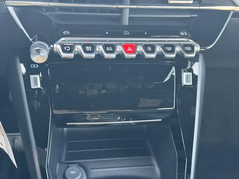 Vue rapprochée de la console centrale noire brillante du Peugeot 2008 1.2 Hybrid avec boutons de commande chromés et rouge d’alerte.