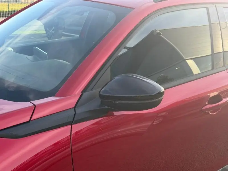 Gros plan sur le rétroviseur noir côté gauche d’un Peugeot 2008 rouge Elixir avec partie avant et vitre teintée visible.