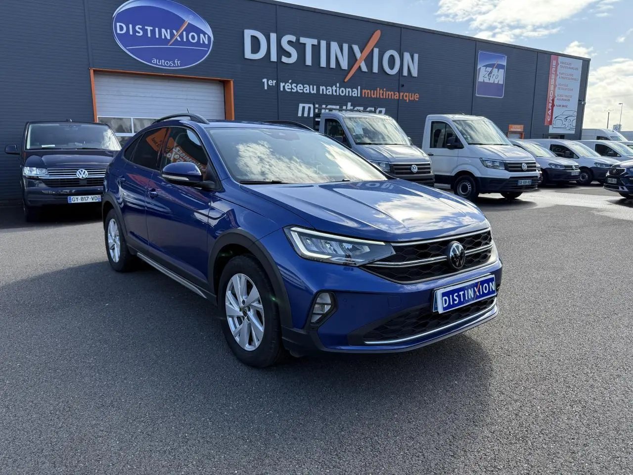 Volkswagen Taigo bleu récif métallisé en 3/4 avant droit sur parking devant concession multimarque Distinxion.