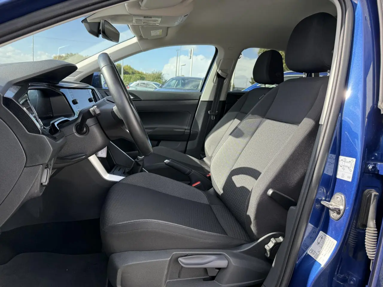 Intérieur côté conducteur du Volkswagen Taigo bleu récif 2024, sièges tissu noirs et tableau de bord moderne.