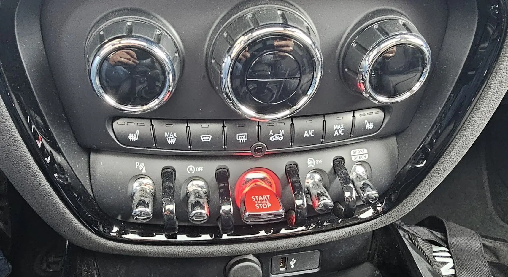 Gros plan sur la console centrale du MINI Clubman grise, mettant en valeur les commandes chromées et le bouton rouge Start/Stop.