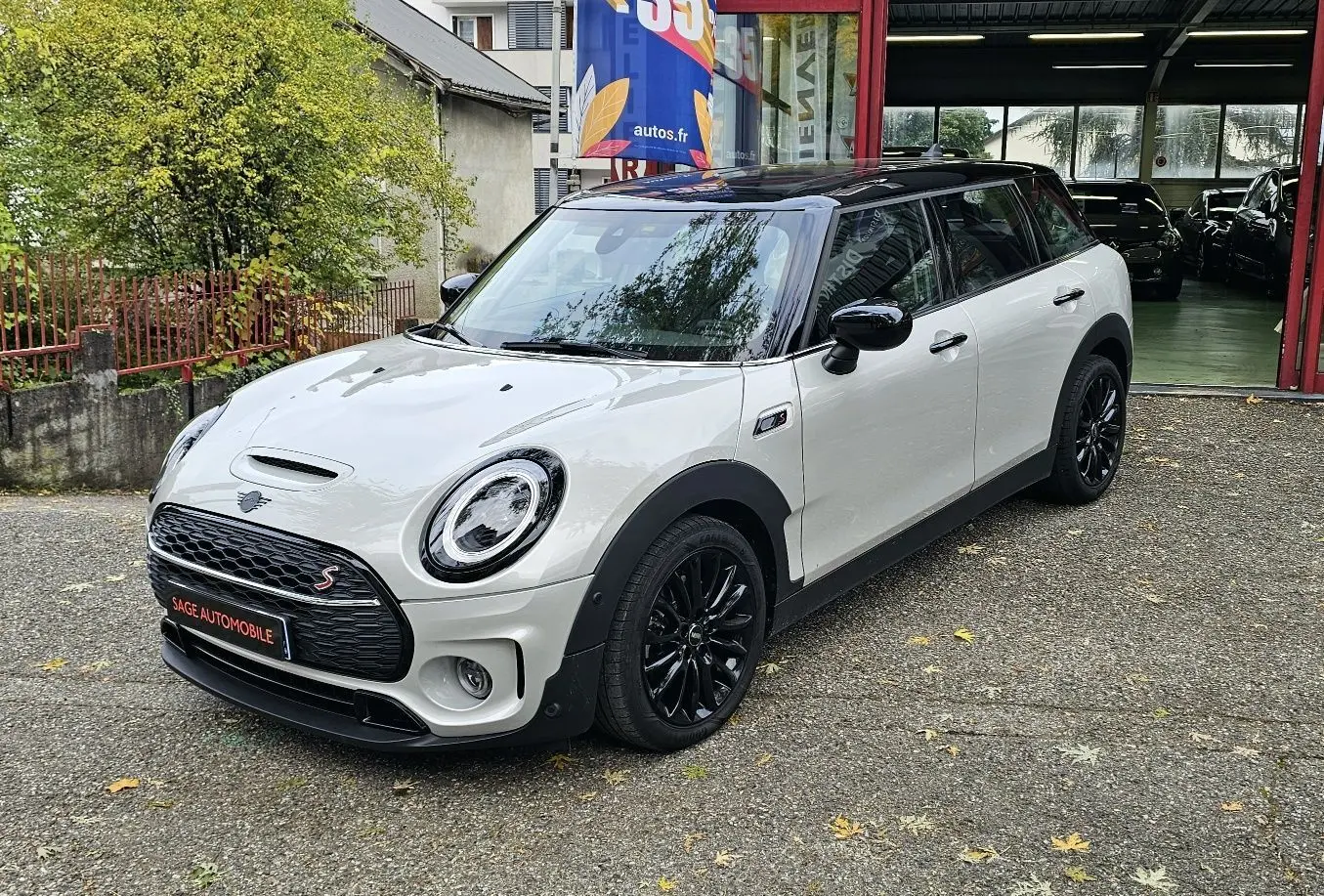 MINI Cooper S Clubman grise vue 3/4 avant droit avec toit noir et jantes noires brillantes stationnée devant un garage.