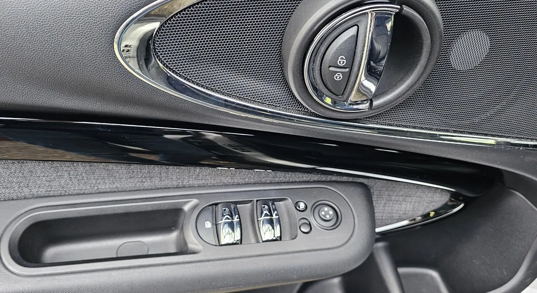Poignée intérieure côté gauche de la MINI Cooper S Clubman 2022 avec commandes de vitres et verrouillage sur garniture noire et tissu gris.