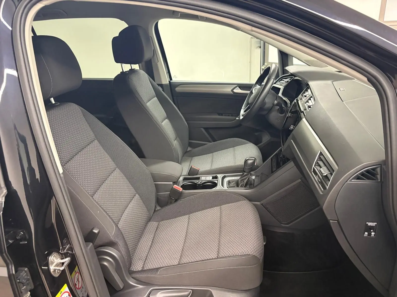 Vue intérieure côté conducteur du Volkswagen Touran 2024 noir intense nacré, montrant sièges et tableau de bord modernes.