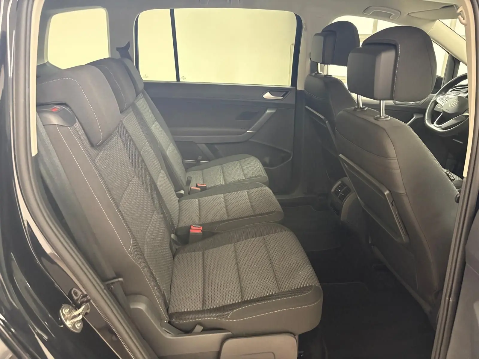 Vue intérieure côté gauche montrant les sièges arrière en tissu gris et l'avant du Volkswagen Touran noir intense nacré 2024.