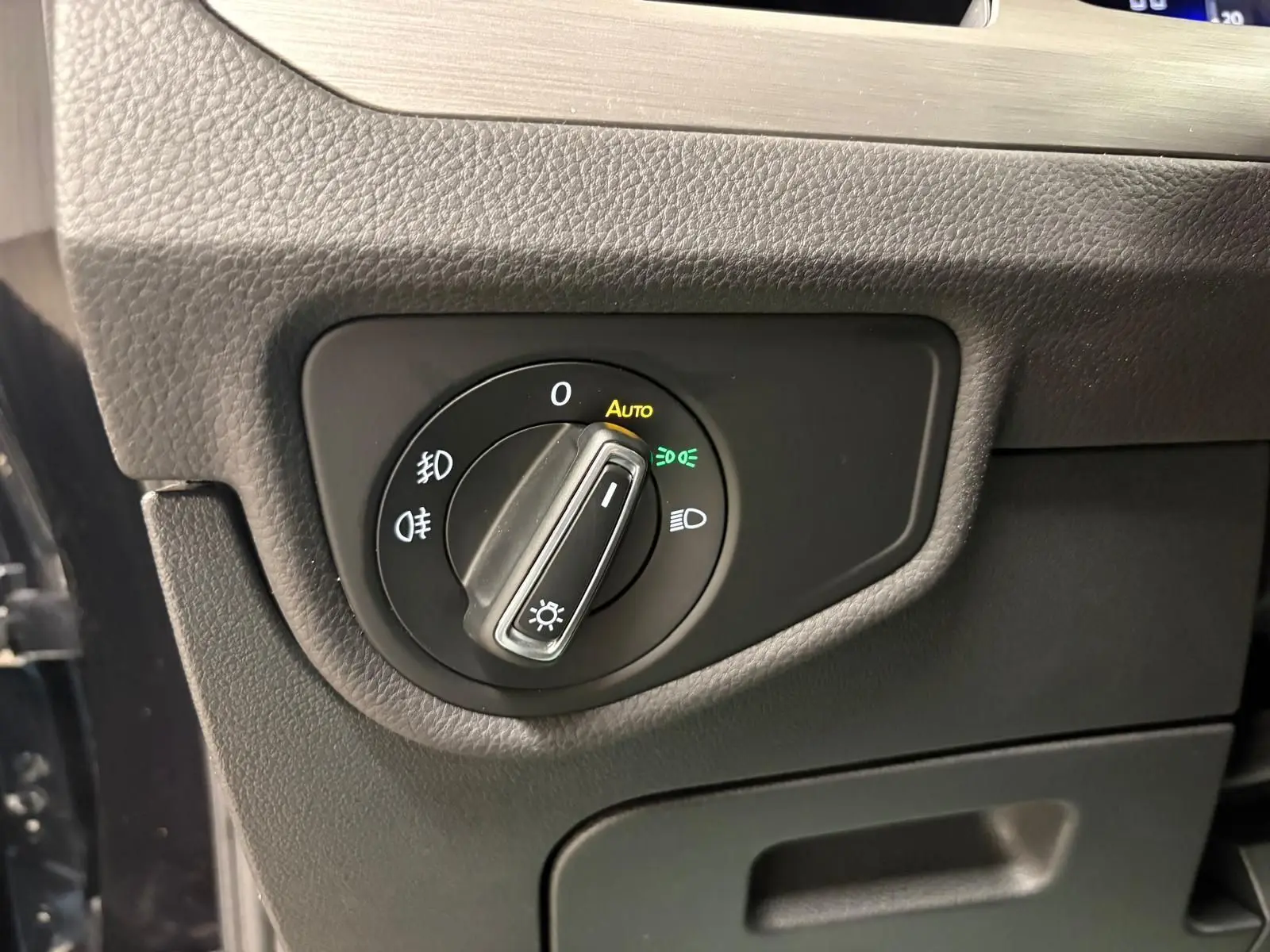 Gros plan sur le bouton de commande des phares du Volkswagen Touran noir intense nacré, intérieur côté conducteur.