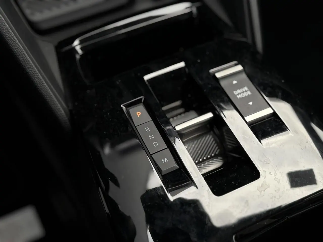 Gros plan sur la console centrale noire brillante de la Citroën C4 Hybrid avec commandes de boîte auto et mode de conduite.
