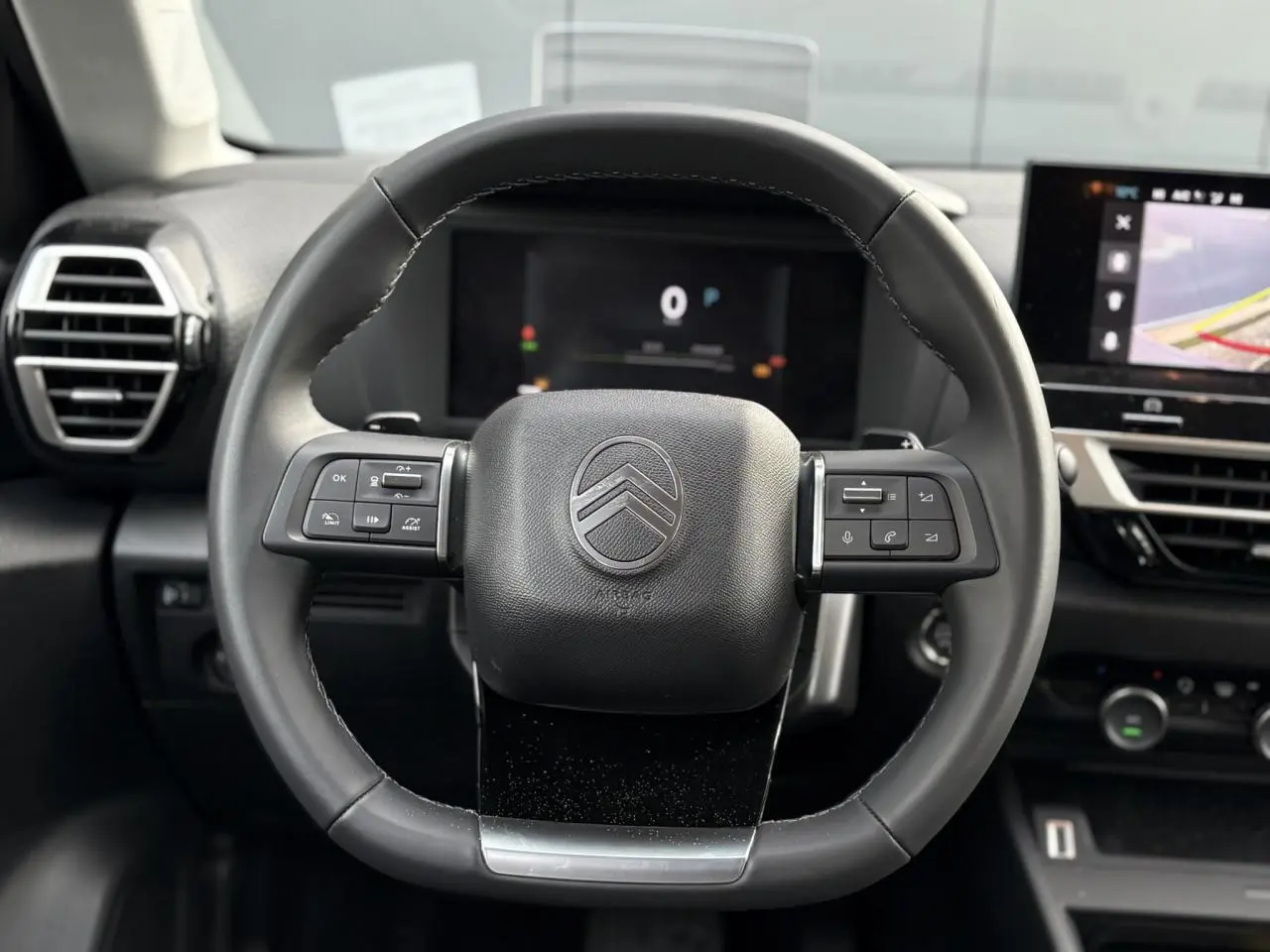 Vue rapprochée du volant cuir noir de la Citroën C4 Hybrid 2025 avec commandes intégrées et tableau de bord numérique.