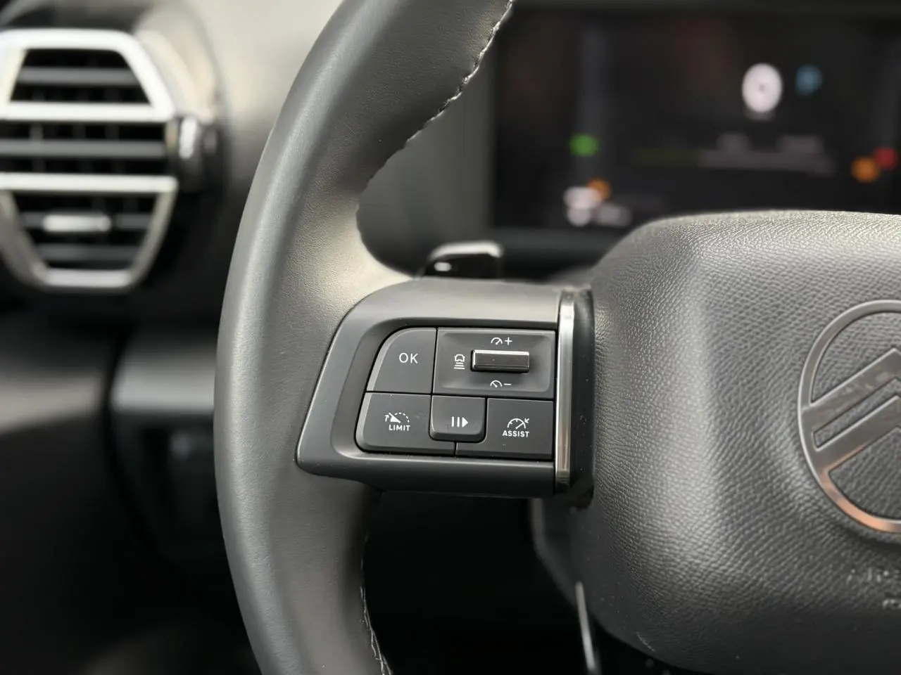 Gros plan sur les commandes au volant côté gauche du Citroën C4 Hybrid gris Mercury, avec aérateur en arrière-plan.