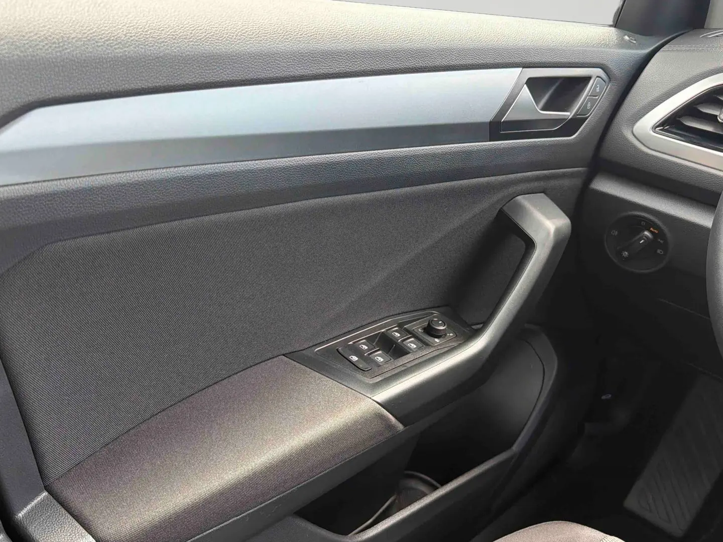 Vue intérieure côté conducteur du panneau de porte noir du Volkswagen T-Roc 2025 avec commandes électriques des vitres et rétroviseurs.
