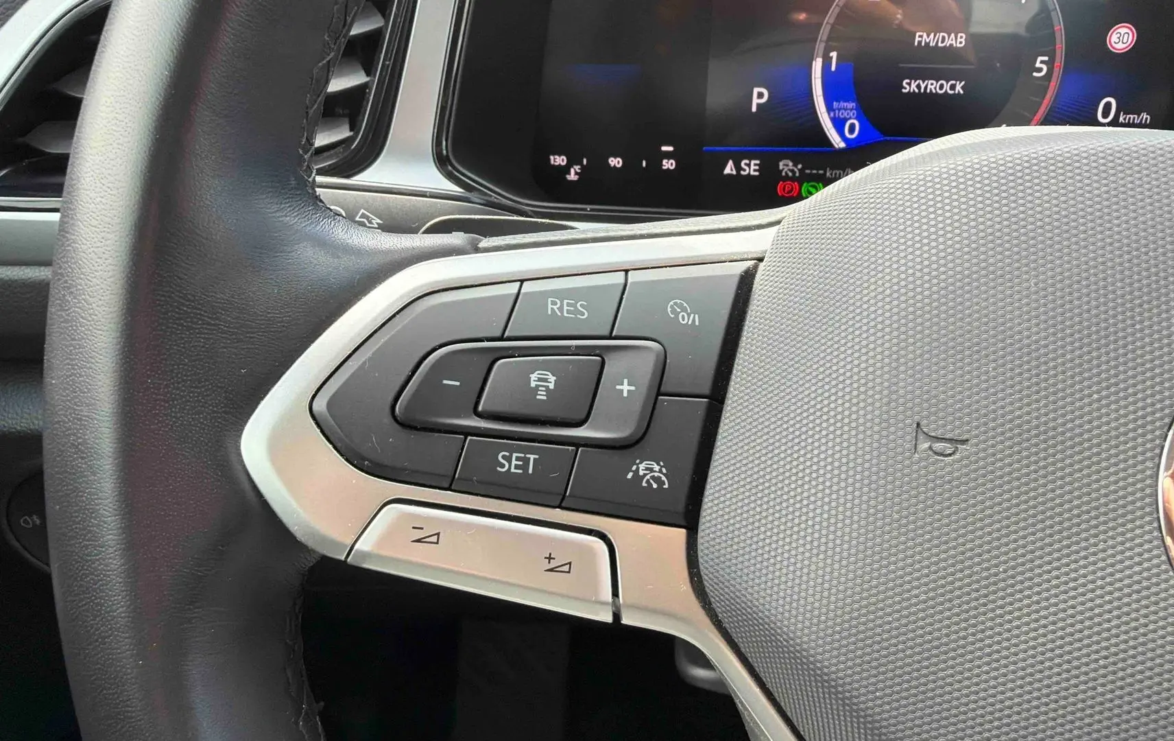 Gros plan sur le volant cuir multifonctions côté gauche du Volkswagen T-Roc noir, avec commandes de régulateur de vitesse.