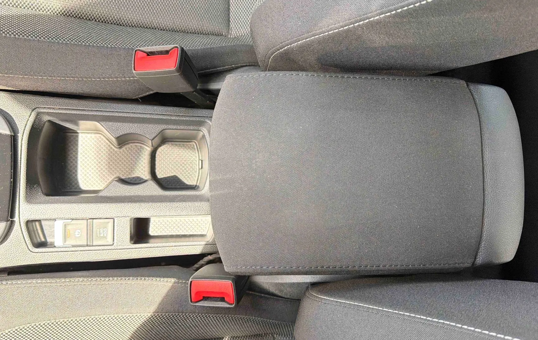 Vue plongeante sur la console centrale noire du Volkswagen T-Roc 2025, avec accoudoir et porte-gobelets.