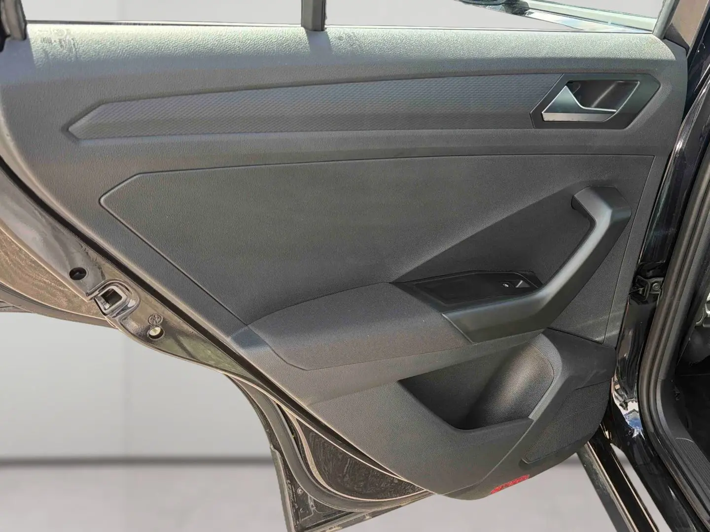 Vue rapprochée de la porte arrière gauche noire du Volkswagen T-Roc 2025, montrant la poignée et les commandes de fenêtre.