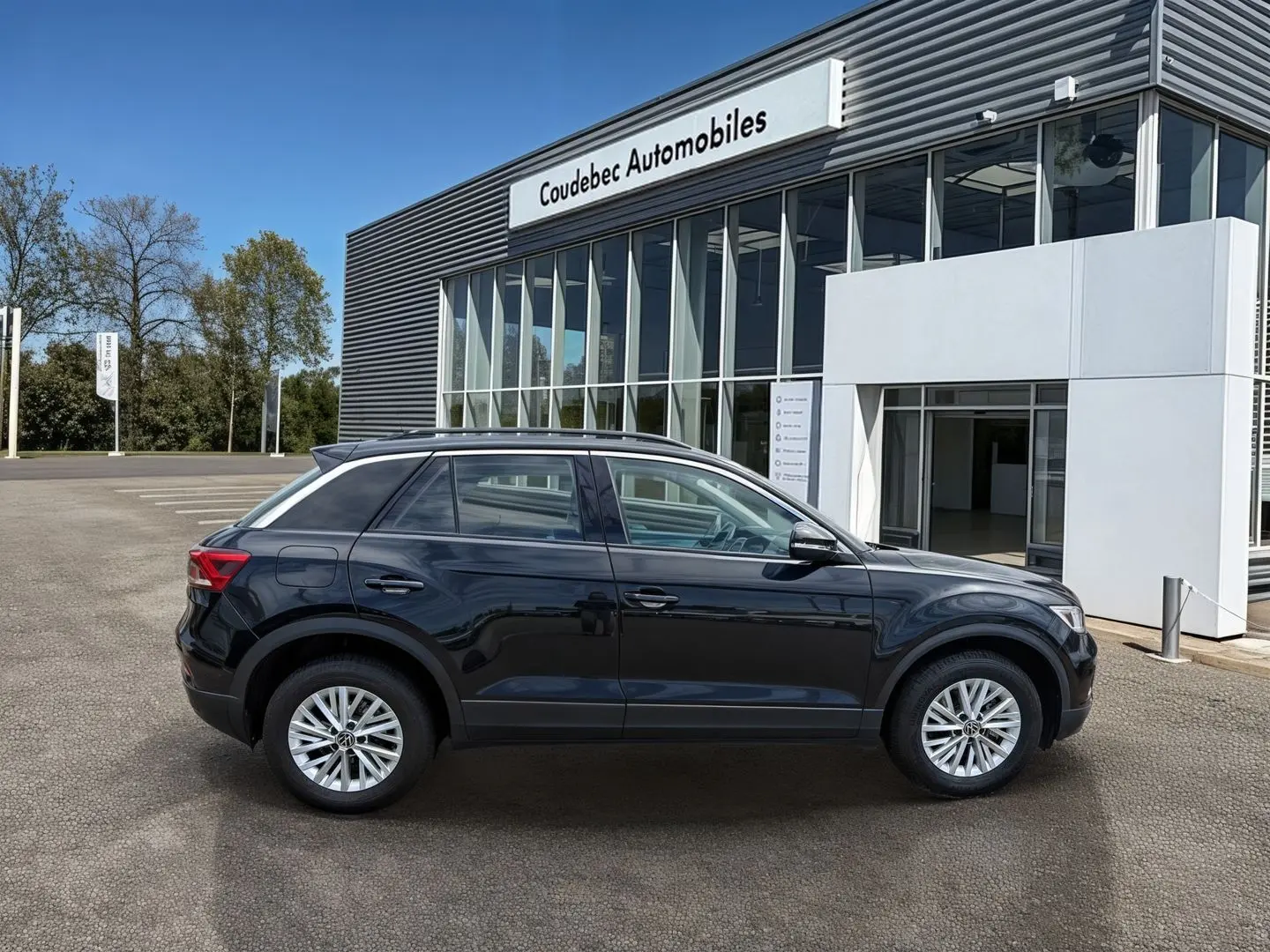 Vue de profil côté gauche d'un Volkswagen T-Roc noir stationné devant un bâtiment commercial.