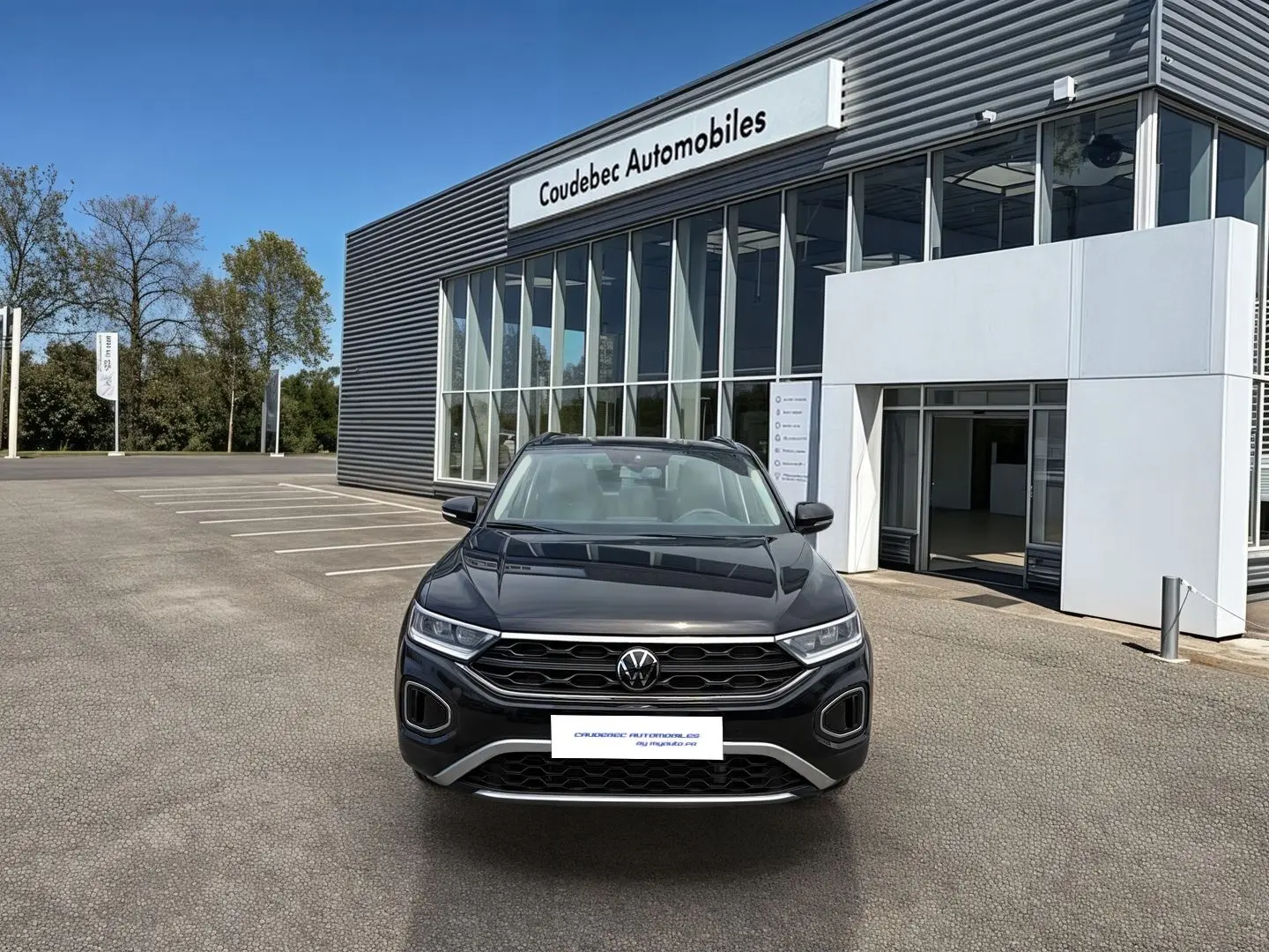 Vue de face du Volkswagen T-Roc noir 2025 garé devant un bâtiment moderne de concession automobile.