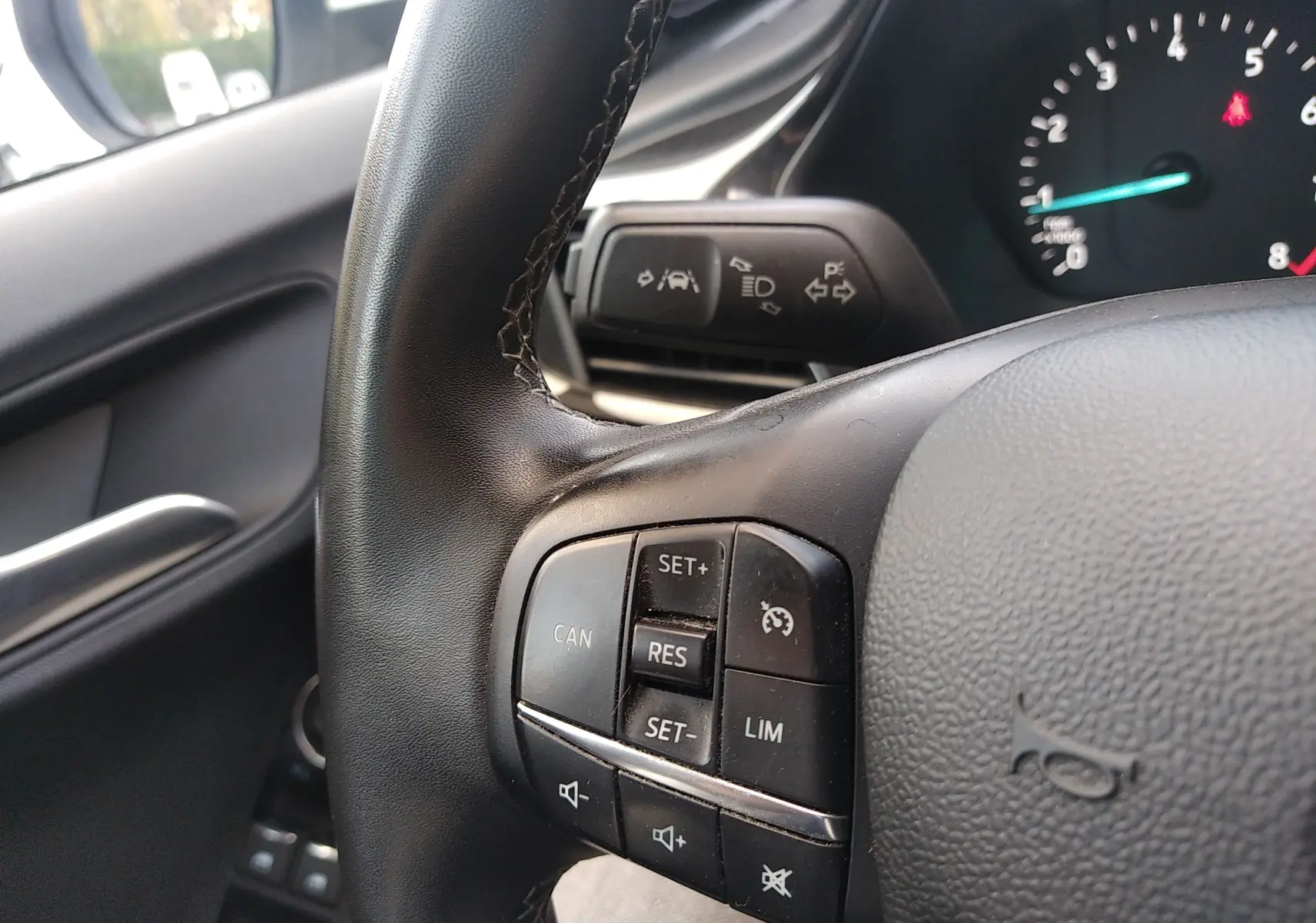 Gros plan sur les commandes au volant noir du Ford Puma 2021, avec tableau de bord et rétroviseur côté gauche en arrière-plan.