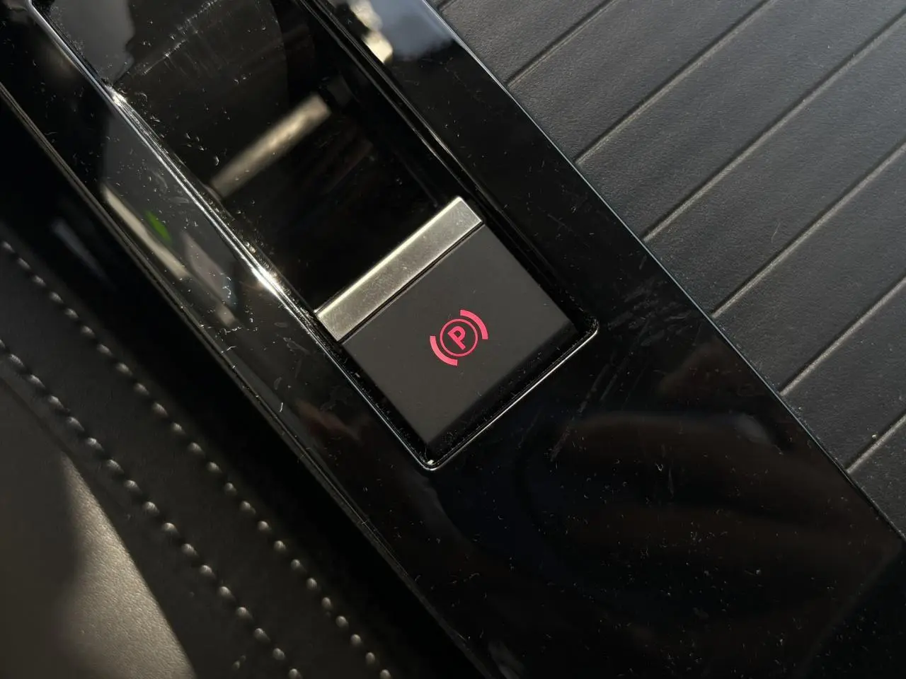 Gros plan sur le bouton de frein de stationnement électrique rouge sur console noire brillante de Citroën C4 Hybrid 2025.