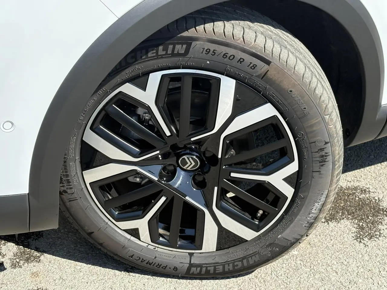 Gros plan sur la roue avant droite d’une Citroën C4 blanche avec jante alliage noire et argentée au design géométrique.