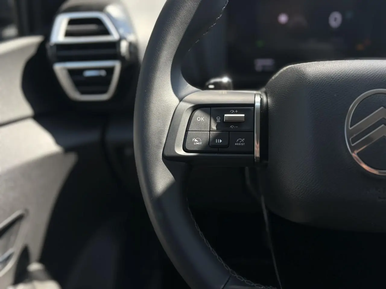 Gros plan sur la partie gauche du volant noir de la Citroën C4 Hybrid 2025 avec commandes intégrées et aérateur en arrière-plan.