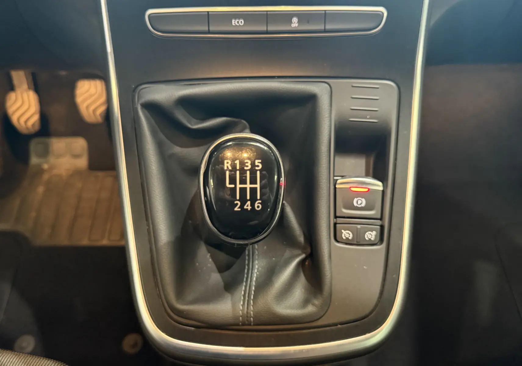 Gros plan sur le levier de vitesse manuel noir du Renault Grand Scenic IV Business, entouré de commandes et d'un bouton de frein à main électrique.