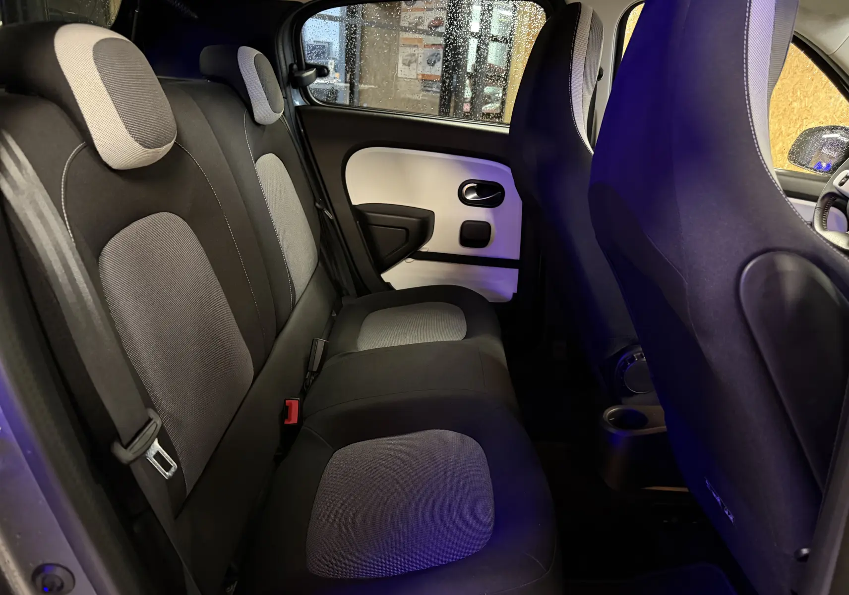 Vue intérieure arrière de la Renault Twingo III gris, montrant les sièges arrière en tissu bicolore et la portière côté gauche.