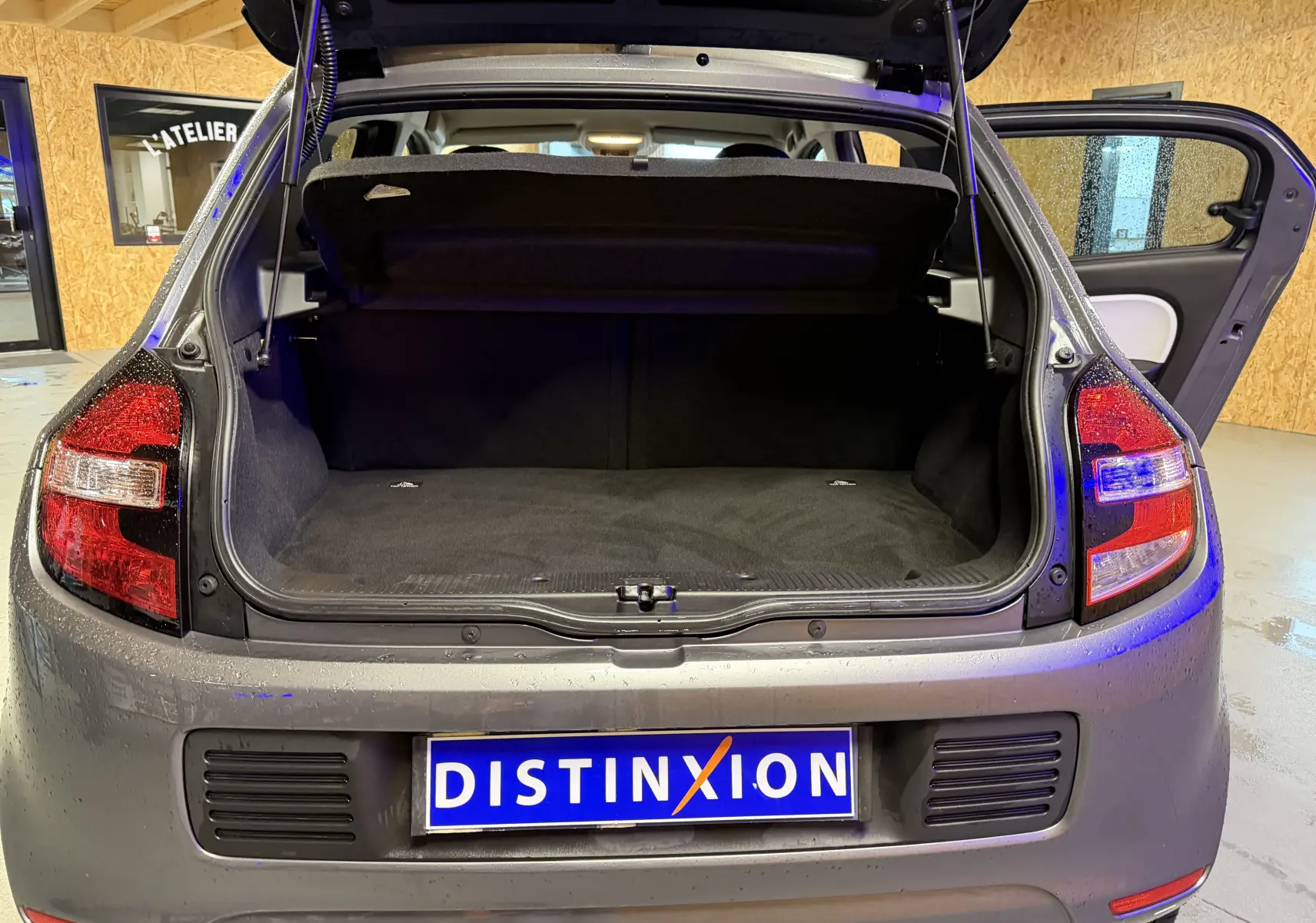 Vue arrière de la Renault Twingo III gris avec coffre ouvert et porte arrière droite entrouverte en intérieur.