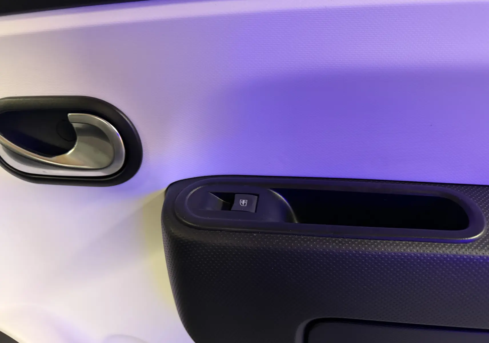 Détail de la poignée intérieure et commande de lève-vitre sur la porte avant d’une Renault Twingo III gris, vue côté droit.