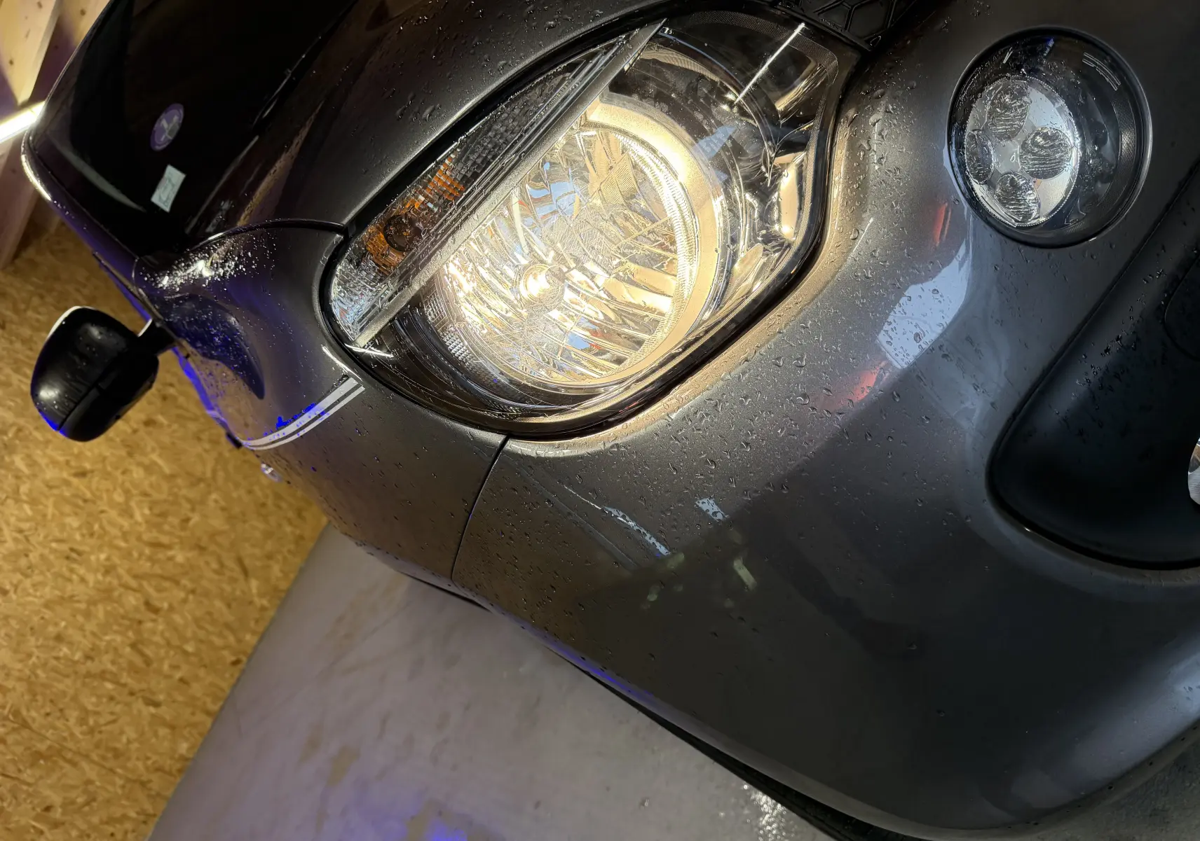 Gros plan sur l'avant droit gris d'une Renault Twingo III 2018, mettant en valeur le phare halogène et le rétroviseur noir.