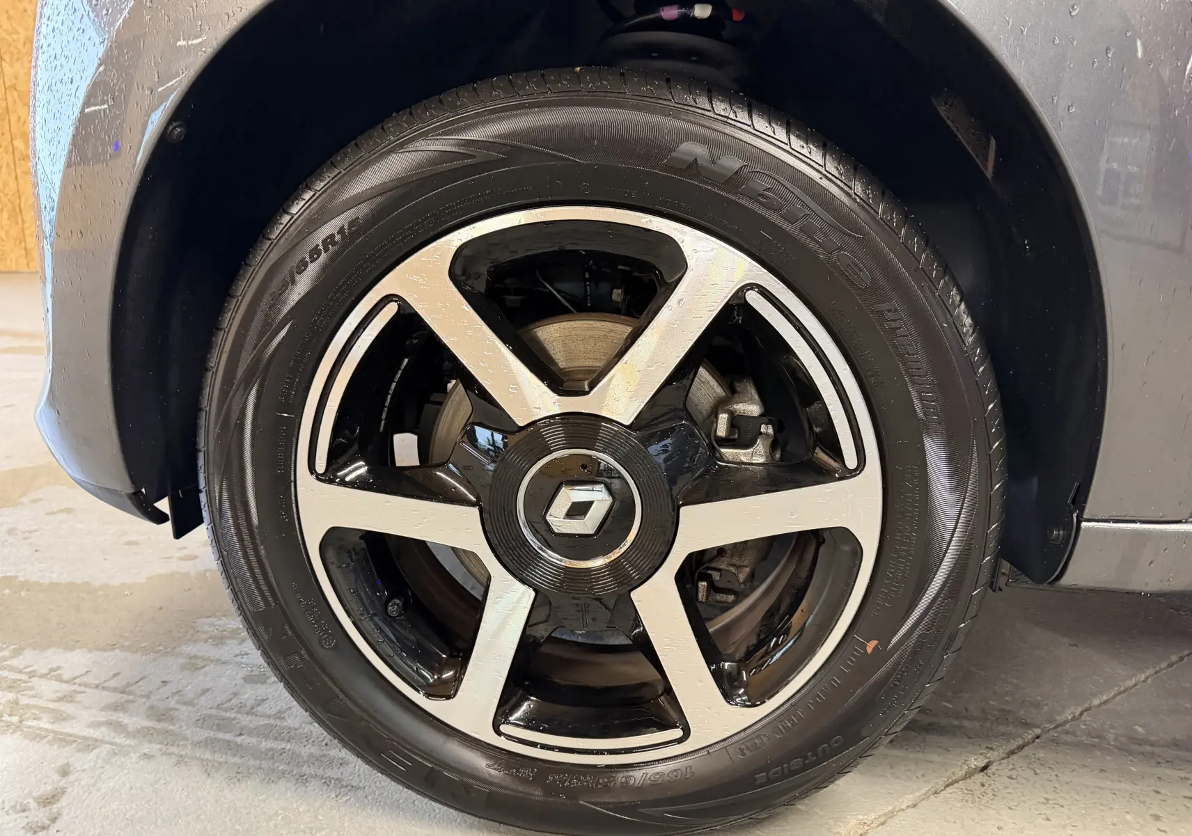 Gros plan sur la roue avant droite d'une Renault Twingo III gris avec jante alliage bicolore et logo Renault central.