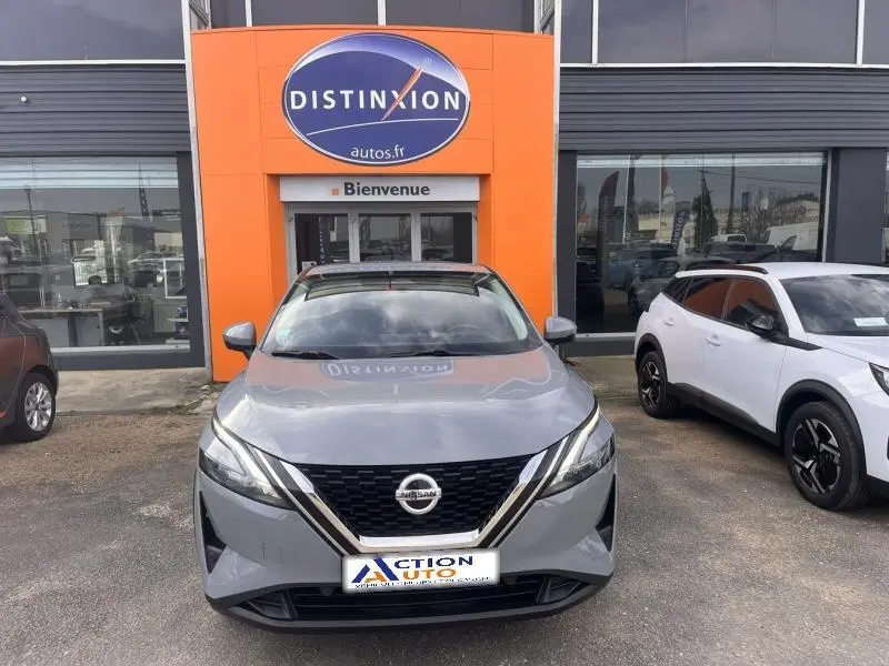 Vue avant d'un Nissan Qashqai 1.3 Mild Hybrid gris argile avec toit noir, garé devant un concessionnaire.