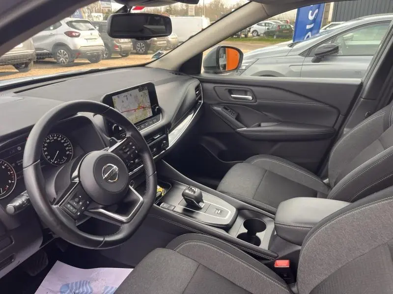 Vue intérieure côté conducteur du Nissan Qashqai 2022, avec tableau de bord noir, écran tactile et sièges tissu gris.