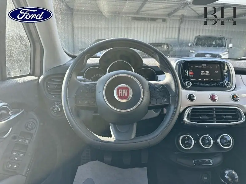 Vue intérieure frontale du tableau de bord et volant cuir noir avec logo FIAT rouge, écran tactile et commandes multifonctions.
