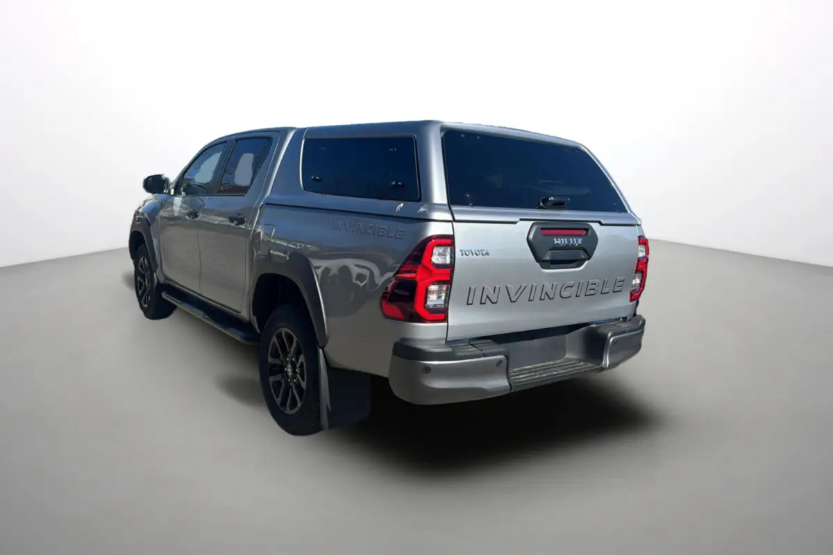 Toyota Hilux 4x4 gris acier en 3/4 arrière droit avec hardtop et logo Invincible visible sur la benne.