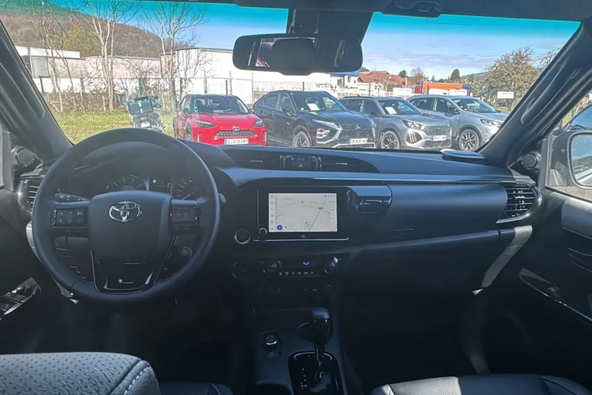 Vue intérieure du Toyota Hilux 2026 montrant le tableau de bord noir avec écran tactile et volant multifonctions.