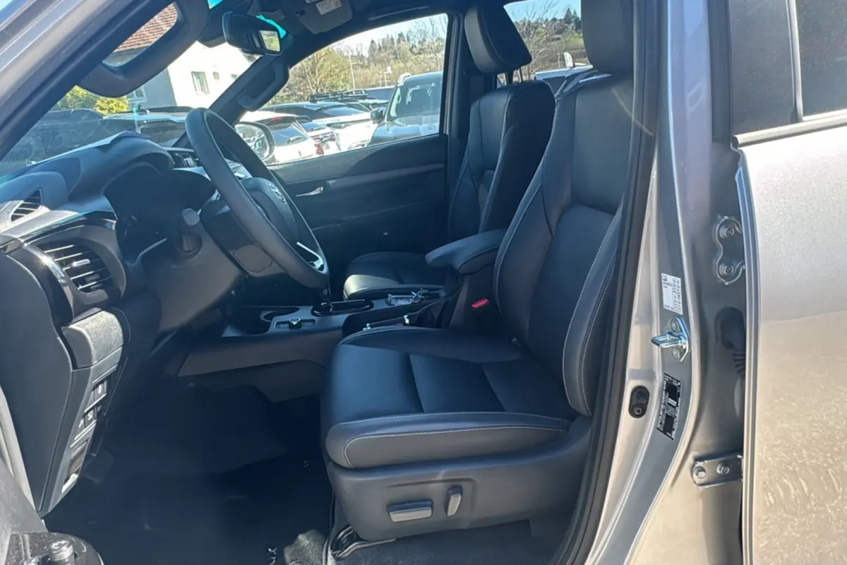 Vue intérieure côté conducteur du Toyota Hilux 2026 gris acier, avec sièges cuir noirs et volant multifonctions.