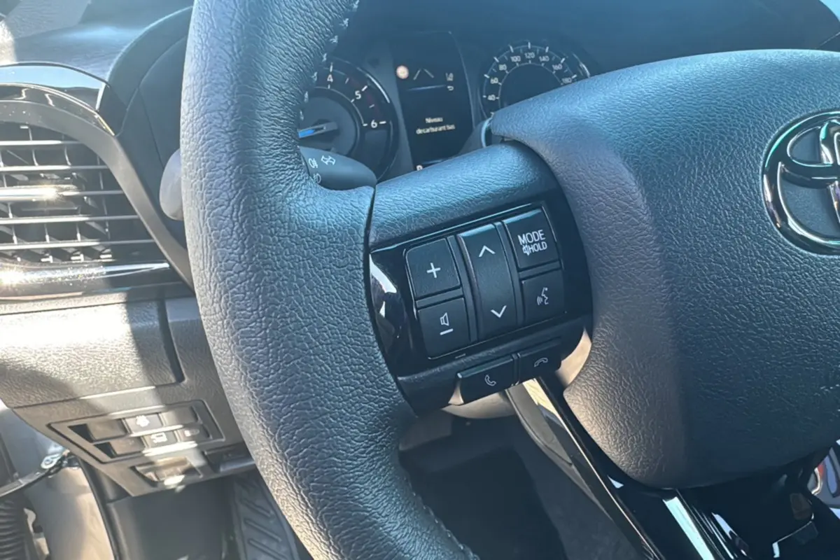 Gros plan sur le volant cuir multifonctions noir du Toyota Hilux 4x4 2026, avec commandes audio intégrées.