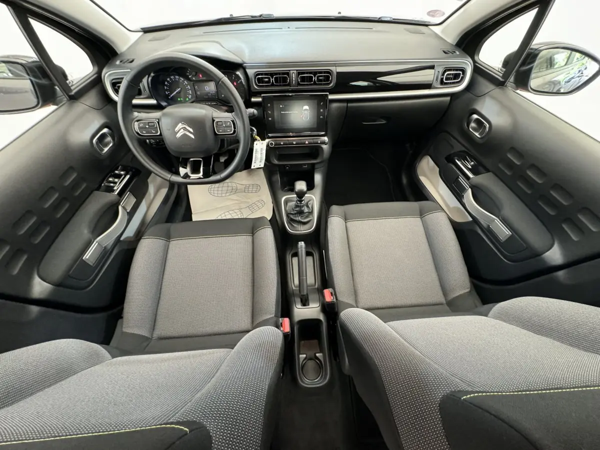 Vue intérieure avant de la Citroën C3 gris foncé, montrant tableau de bord, volant cuir multifonctions et sièges tissu gris.