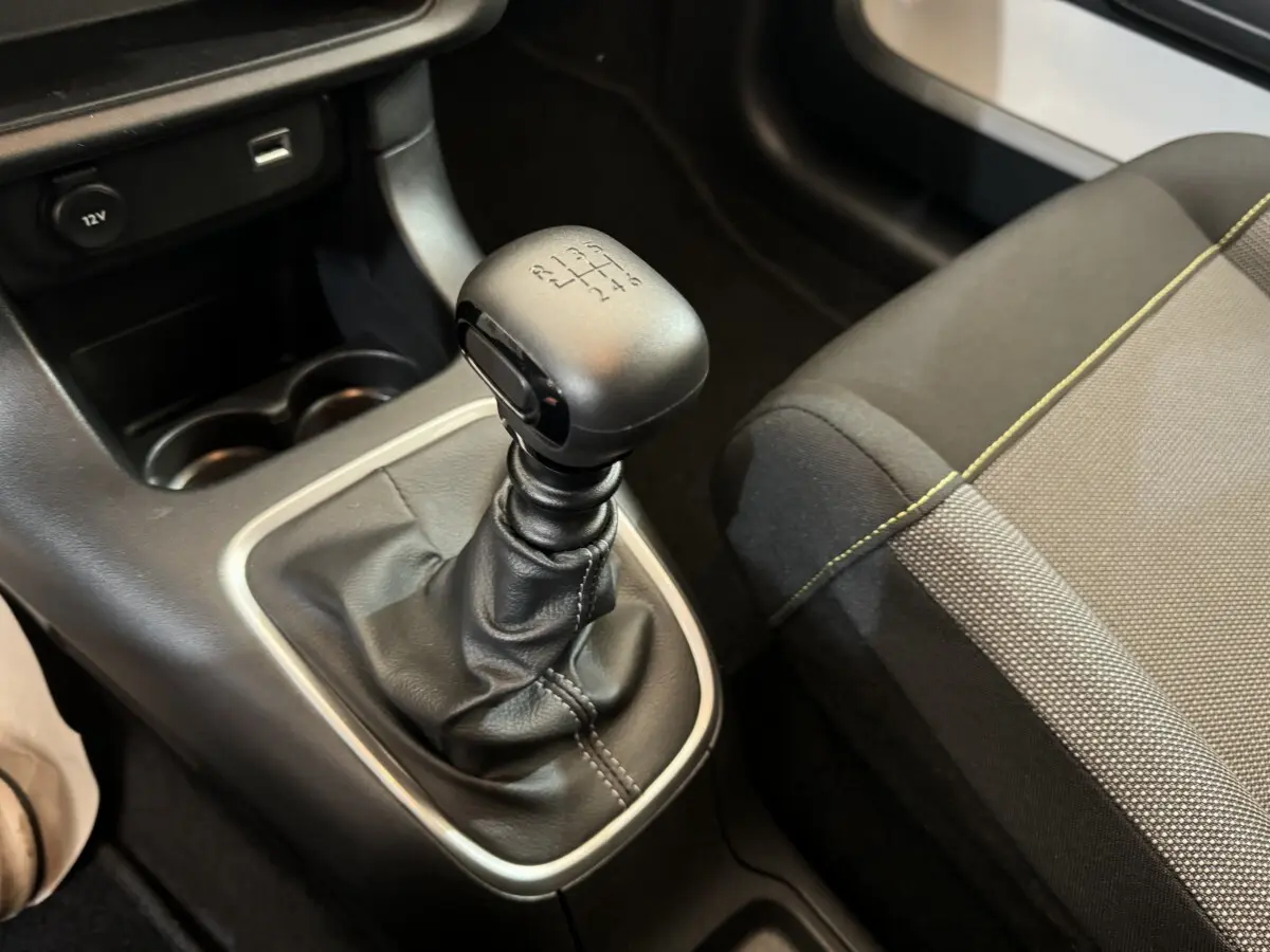 Gros plan sur le levier de vitesse manuel en cuir noir et la console centrale d’une Citroën C3 gris foncé, siège tissu visible.
