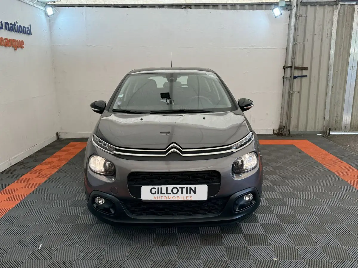 Citroën C3 gris foncé vue de face, avec feux allumés et calandre noire distinctive.