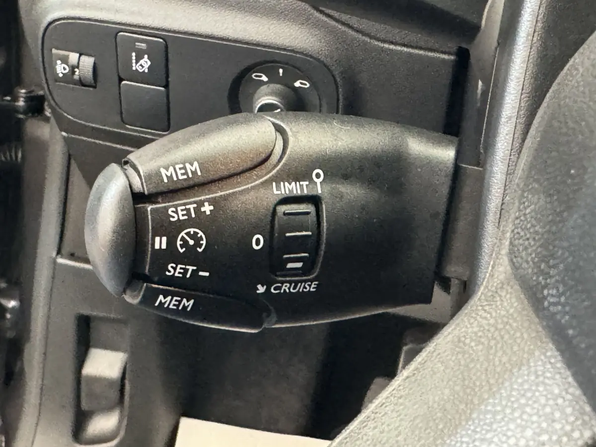 Gros plan sur la commande de régulateur de vitesse du côté gauche du volant cuir d'une Citroën C3 gris foncé 2020.