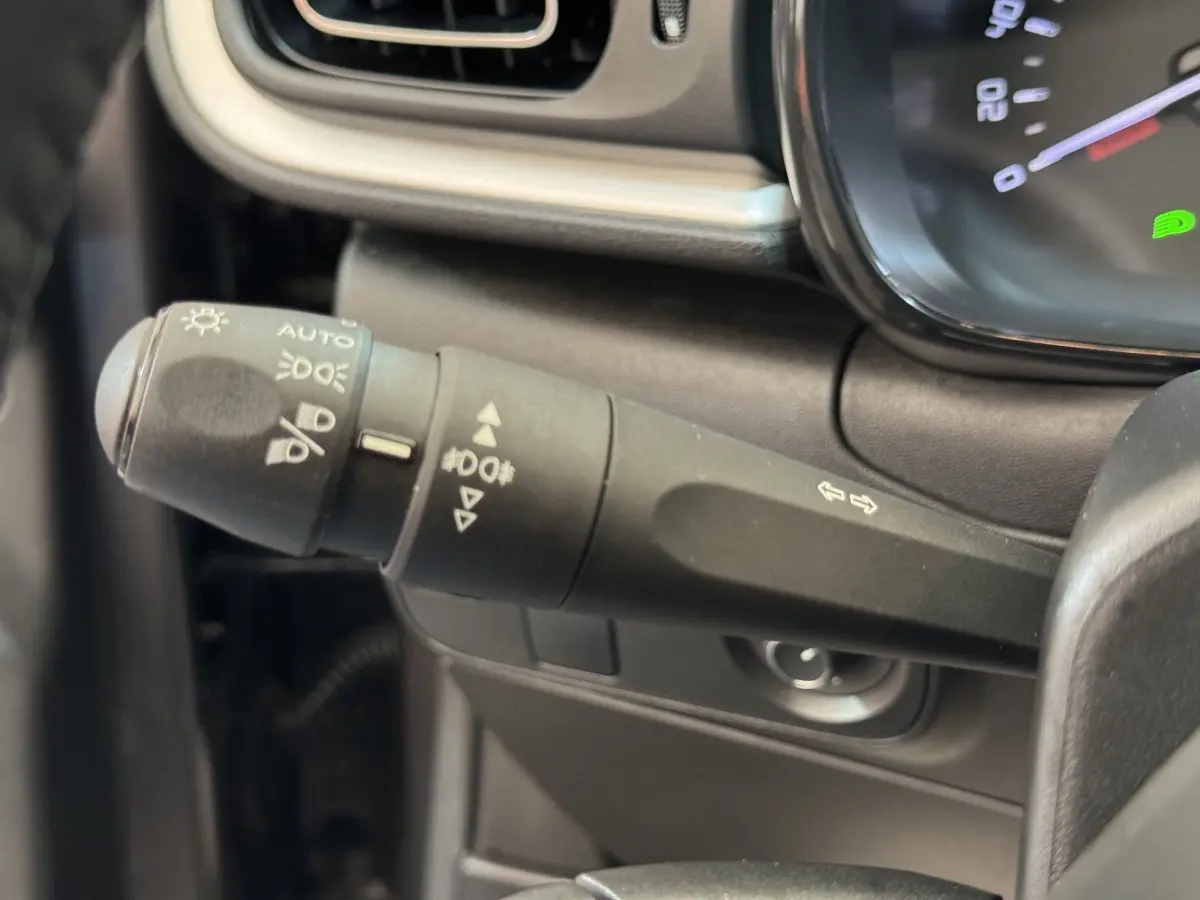 Gros plan sur la commande des phares et clignotants à gauche du volant cuir dans l’habitacle gris foncé du Citroën C3 2020.