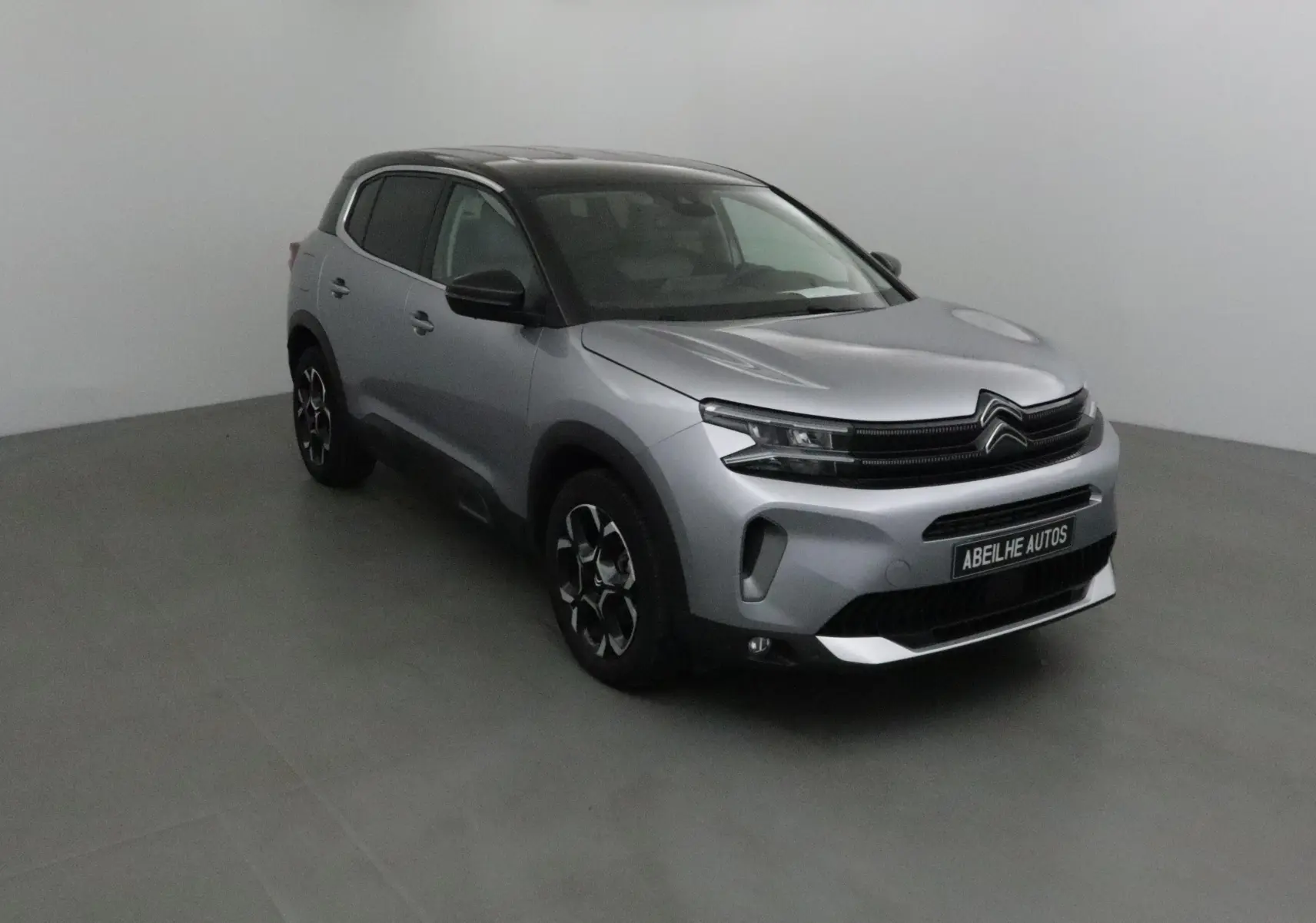 Citroën C5 Aircross 2024 gris Artense avec toit noir, vue 3/4 avant droit en intérieur neutre.