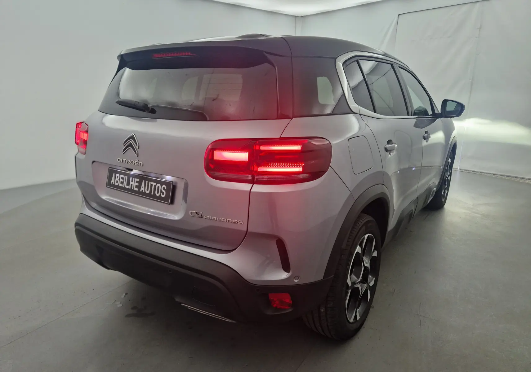 Vue 3/4 arrière droite du Citroën C5 Aircross gris Artense avec feux arrière allumés et toit noir contrastant.