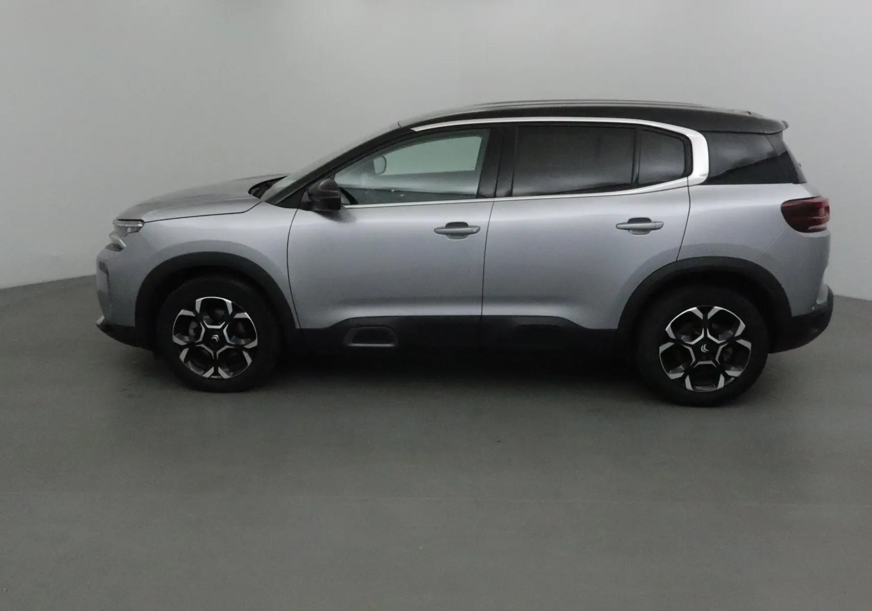 Profil côté gauche du Citroën C5 Aircross 2024 gris Artense avec toit noir et protections noires sur les bas de caisse.