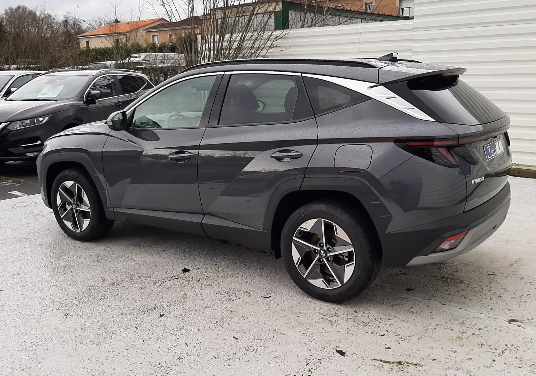 Vue 3/4 arrière gauche d'un Hyundai Tucson 2025 gris Ecotronic avec hayon électrique et jantes bi-ton.