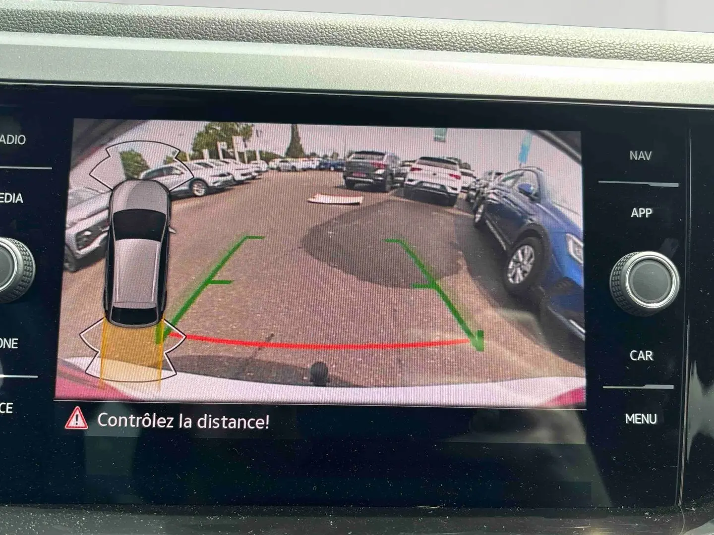 Vue écran caméra de recul du Volkswagen Taigo blanc, avec guidage de trajectoire et alertes de distance visibles.