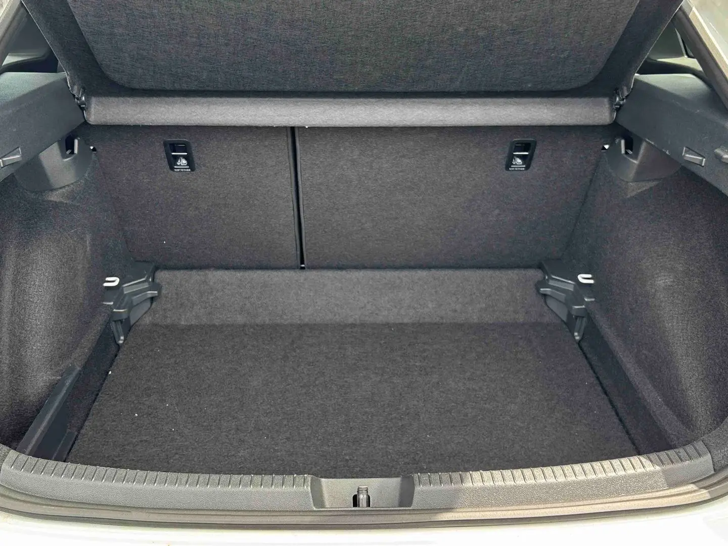 Coffre ouvert vu de l'arrière d'un Volkswagen Taigo blanc, montrant l'espace de chargement vide et la moquette grise.