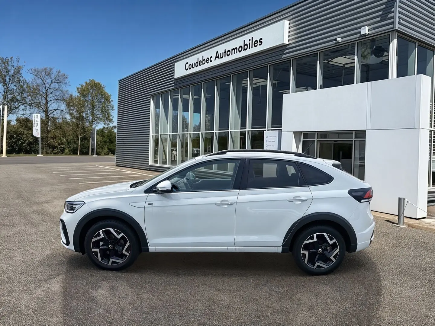 Profil droit d'un Volkswagen Taigo blanc 2025 avec jantes alliage et seuils de porte R-Line devant un concessionnaire.