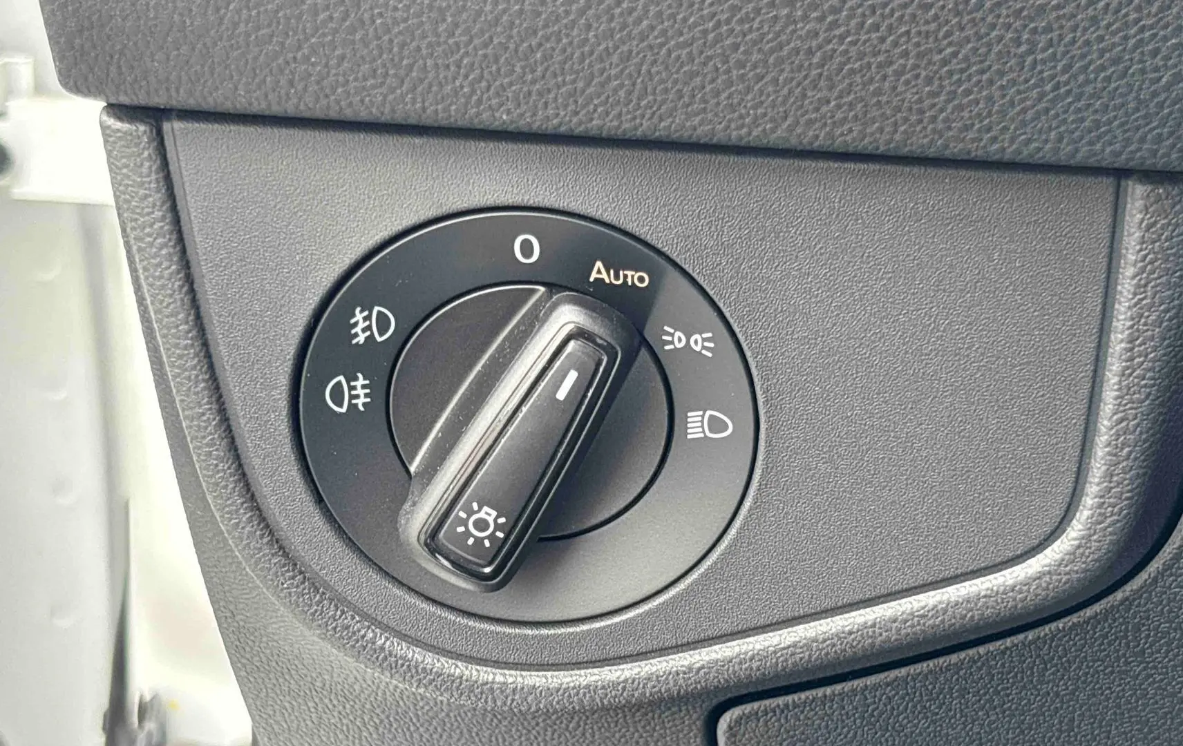 Gros plan sur le bouton de commande des phares dans l’habitacle du Volkswagen Taigo blanc, côté gauche.