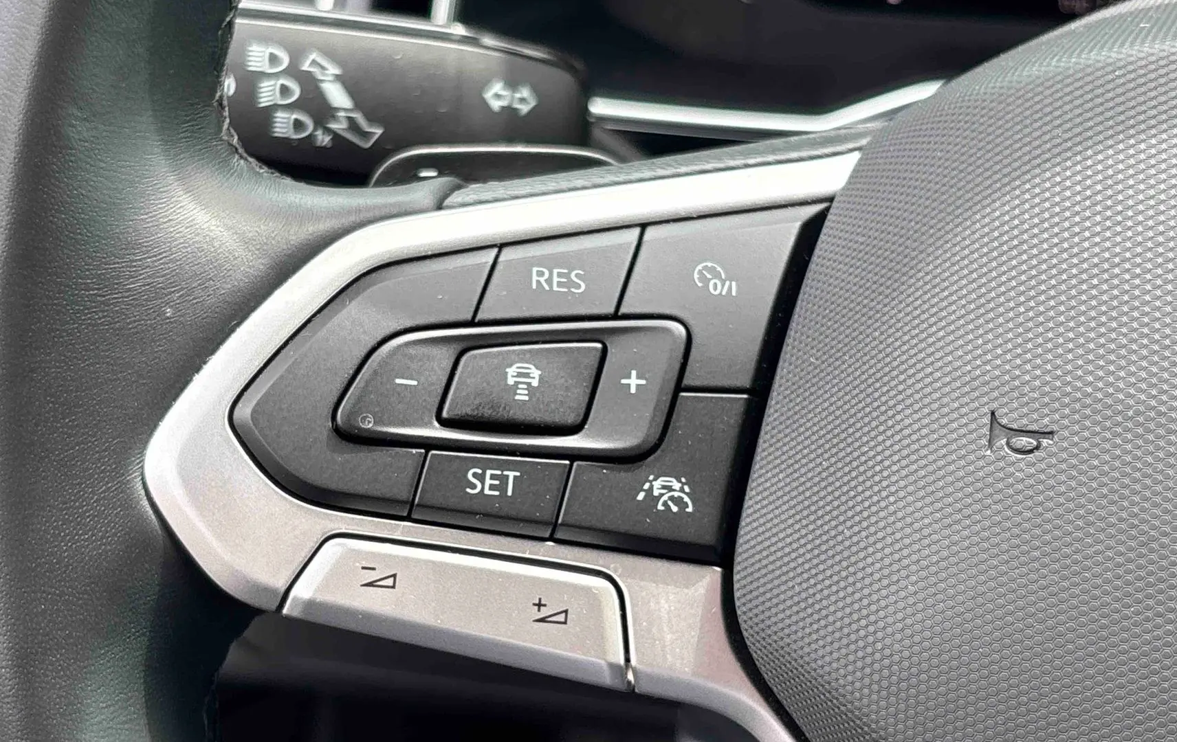 Gros plan sur les commandes multifonctions à gauche du volant en cuir du Volkswagen Taigo blanc, avec boutons de régulateur de vitesse.